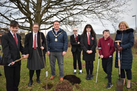 image of five post primary students planting a tree watched by the Mayor Newtownabbey, Mark Cooper and the school Principal Doctor C Scully.