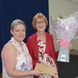 Photograph of a retiring teacher receiving a  bouquet of flowers from a representative  of Jordanstown Together