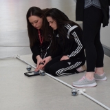 Photograph of a pupil being assisted by a staff member to control a sphere shaped  robot with an iPad